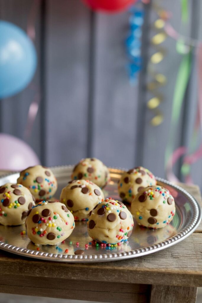 Bite-sized cookie dough balls topped with chocolate chips and sprinkles on a chilled tray