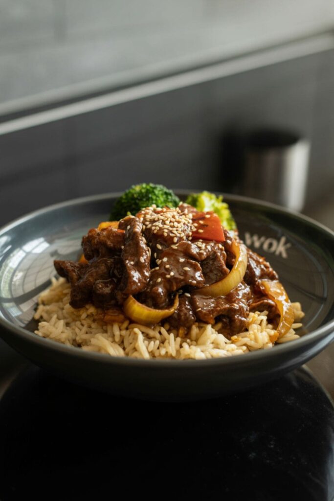 Black pepper beef bowl with onions and steamed rice, topped with sesame seeds