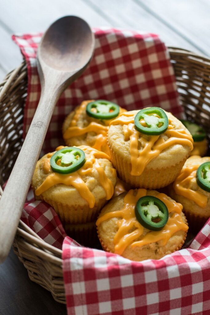 Cheddar jalapen cornbread muffins served in a basket with visible cheese and pepper pieces