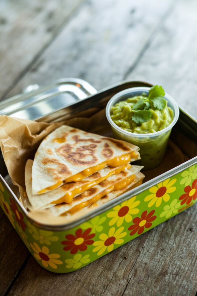 Cheese quesadilla slices arranged in a lunchbox with a side of dipping sauce