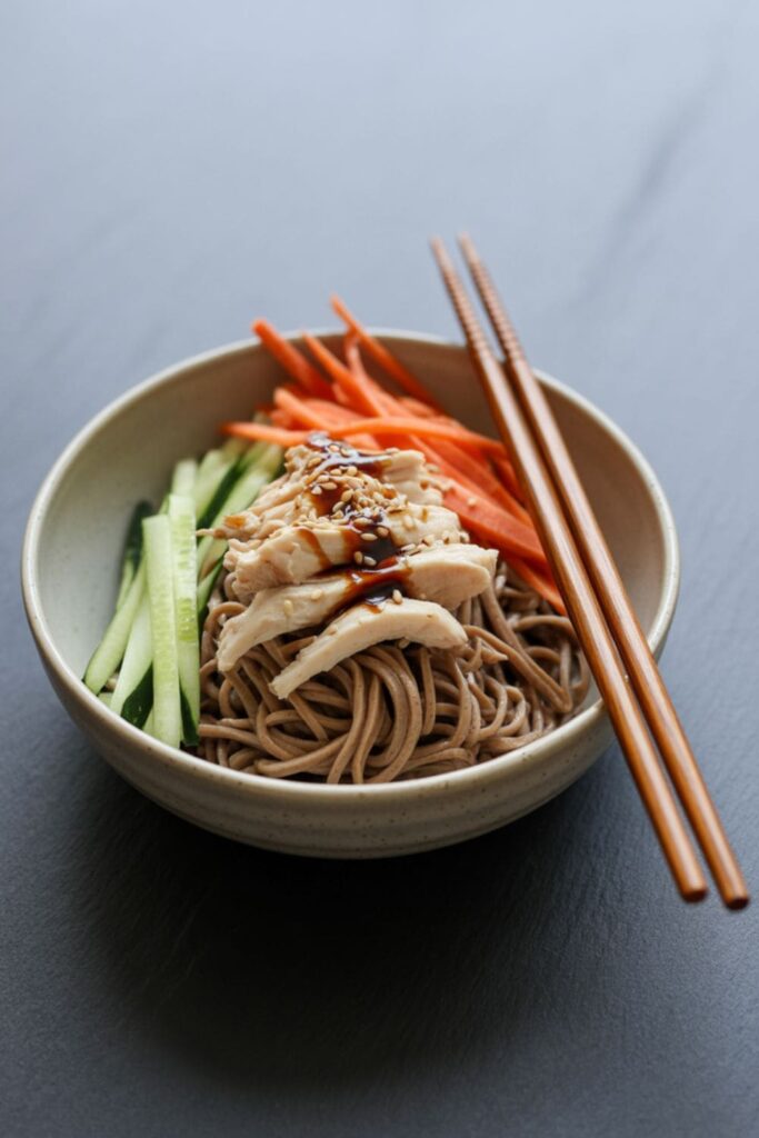 Cold soba noodle salad with chicken, carrots, cucumbers, and sesame seeds in a bowl
