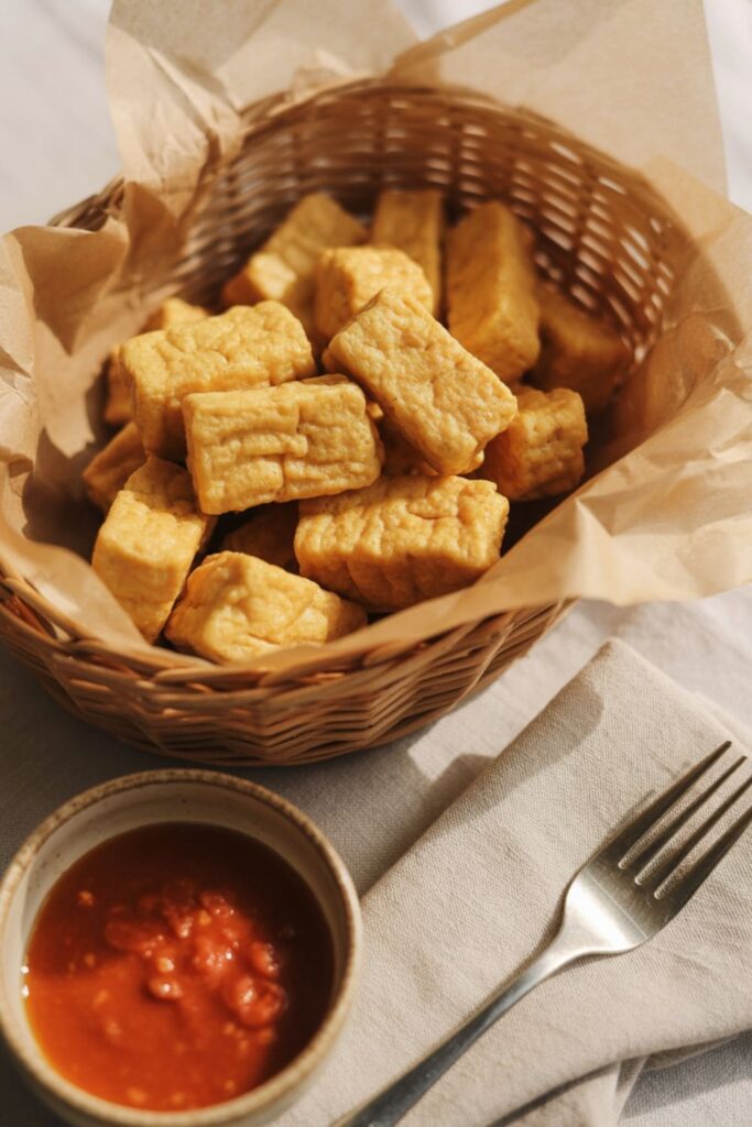 Crispy baked tofu nuggets with dipping sauce served in a parchment-lined basket