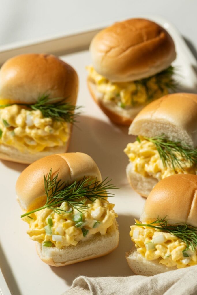 Egg salad sandwich bites cut into small quarters and served on a tray for a party