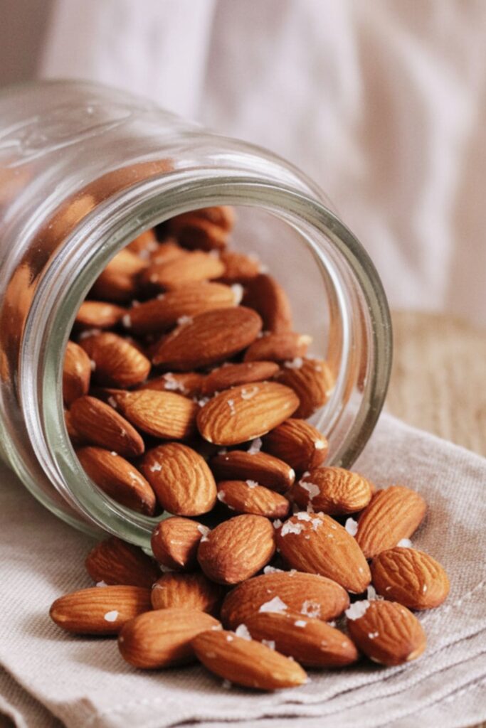 Glass jar spilling roasted almonds onto a napkin with visible sea salt