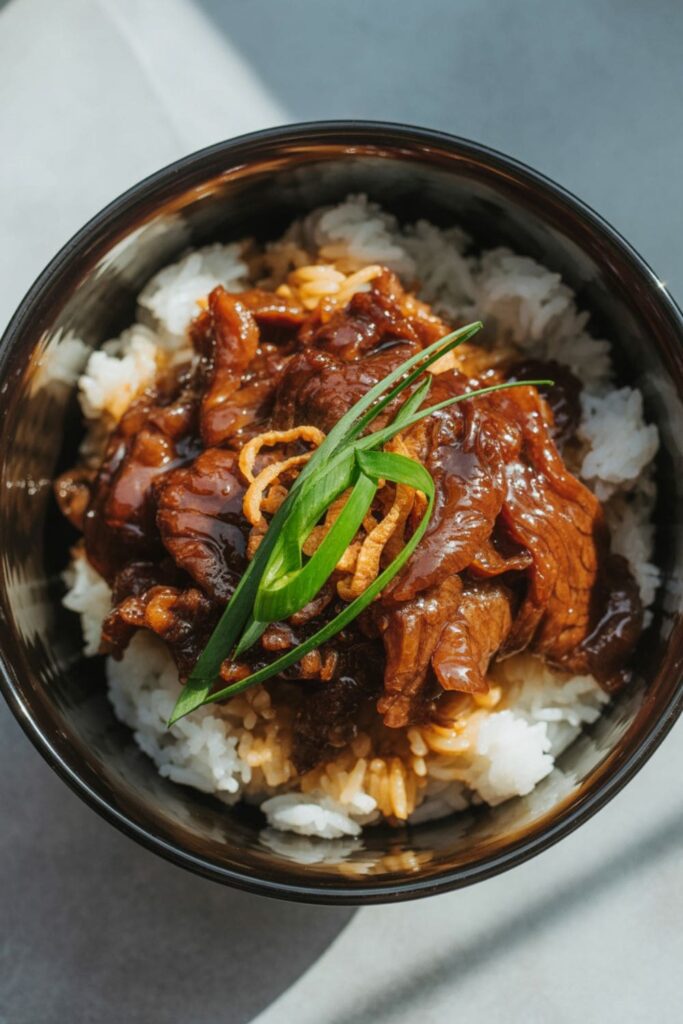 Mongolian beef bowl with green onions and fried onions on top of sticky rice