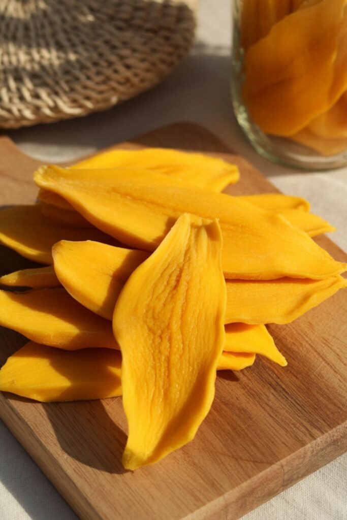 Pile of dried mango slices on a wooden surface with a resealable bag nearby
