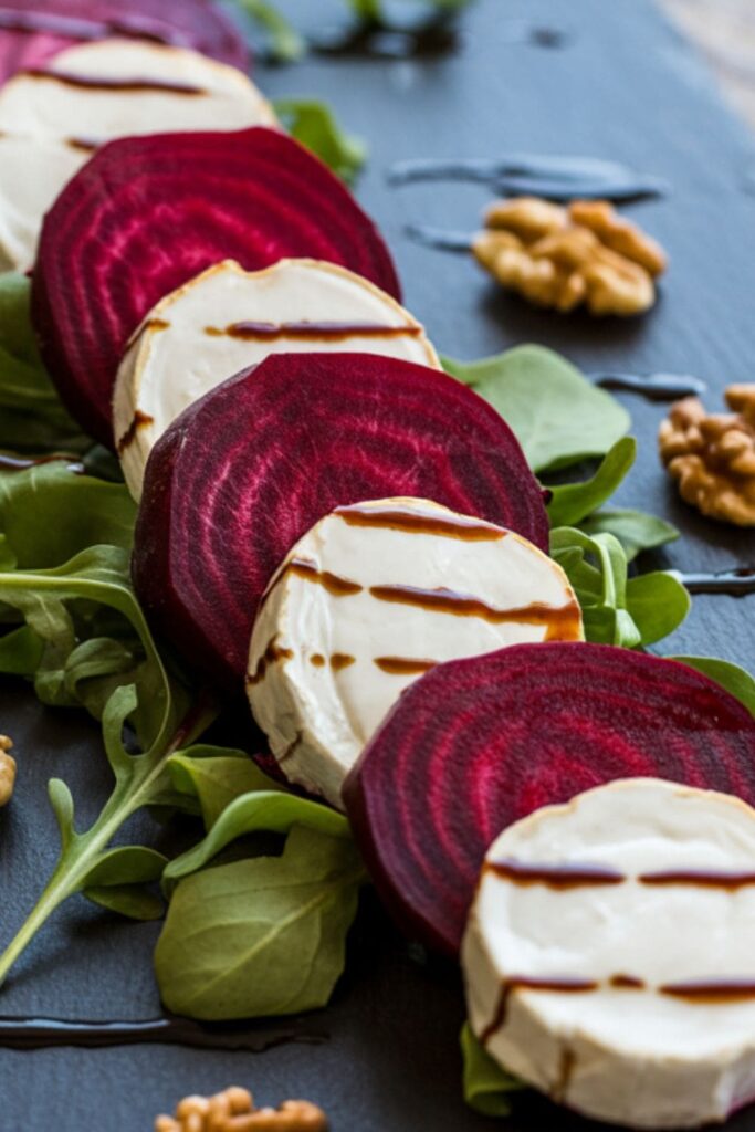 Roasted beet and goat cheese platter with arugula and balsamic drizzle on a black slate