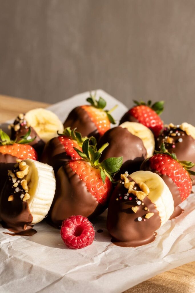 Strawberries and banana slices dipped in chocolate and topped with sprinkles and nuts